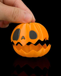 Hand lifting the top half of an orange pumpkin with a jagged opening on a black background