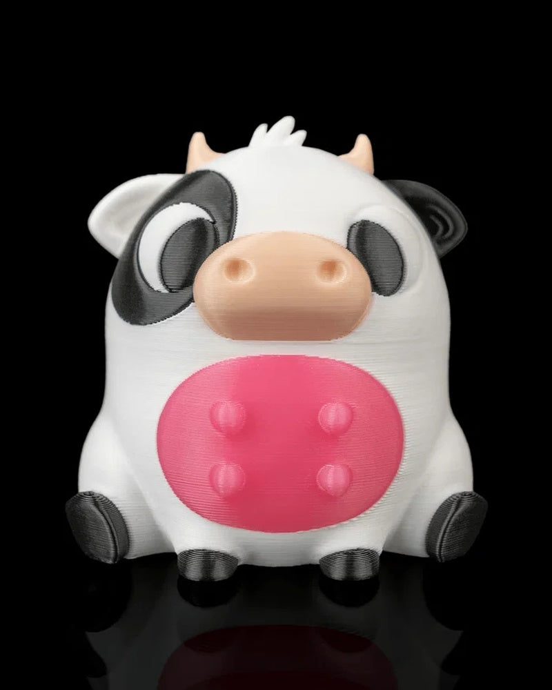 Front view of a round cow figurine with black-and-white markings, peach snout, small horns, and pink belly on a black background.