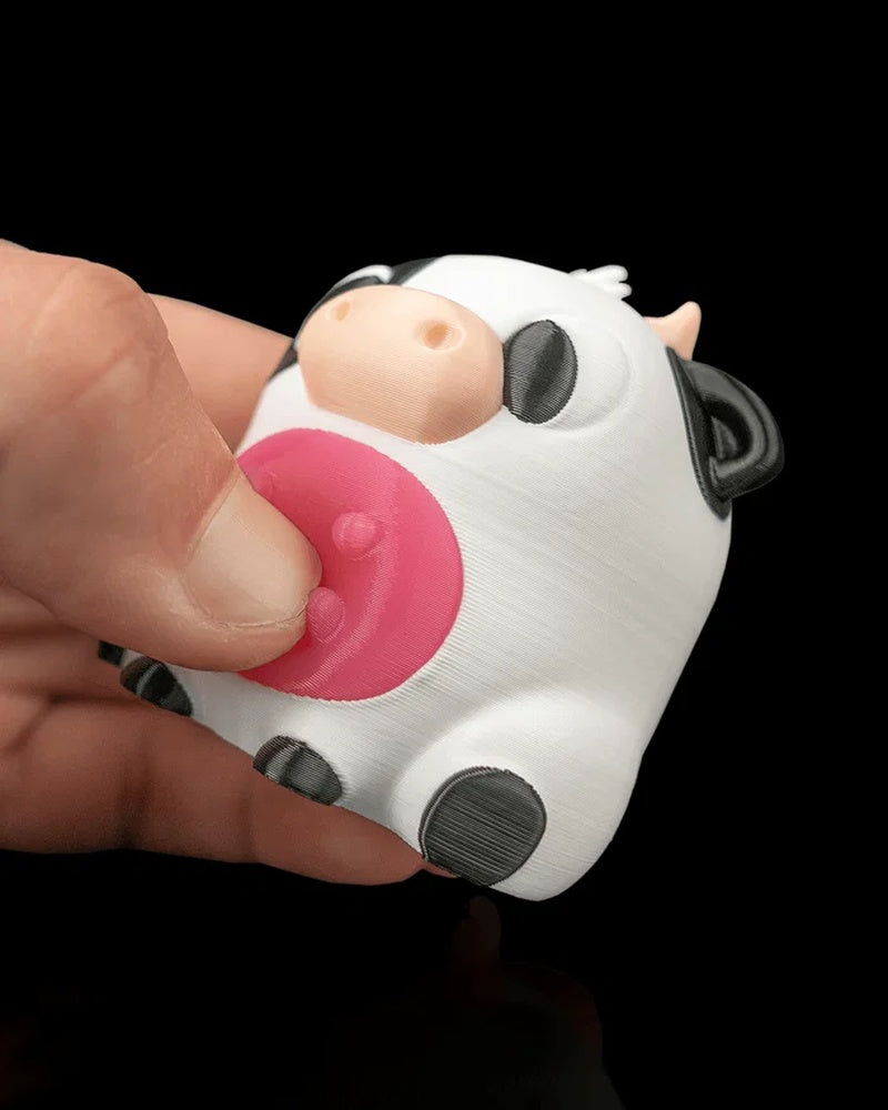 Close-up of a hand pressing the pink belly of a round cow figurine with black-and-white markings.