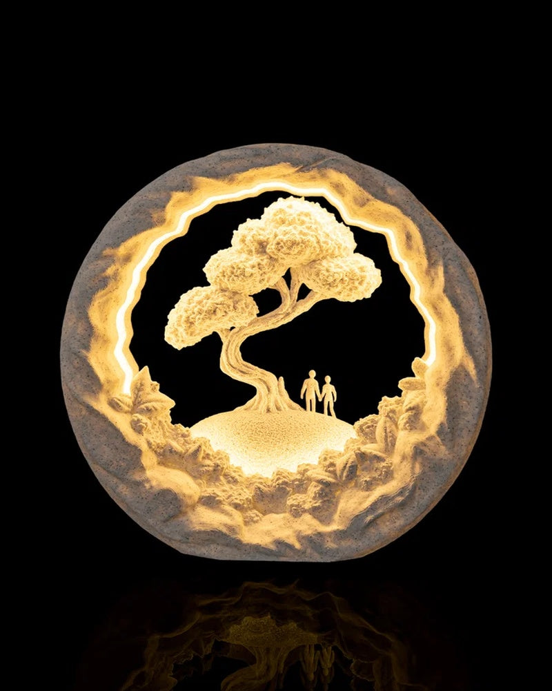 Round illuminated table lamp with a tree, rocky border, and two small figures on a black background