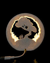Back view of a round lamp with a tree silhouette, warm light, and a visible power cord