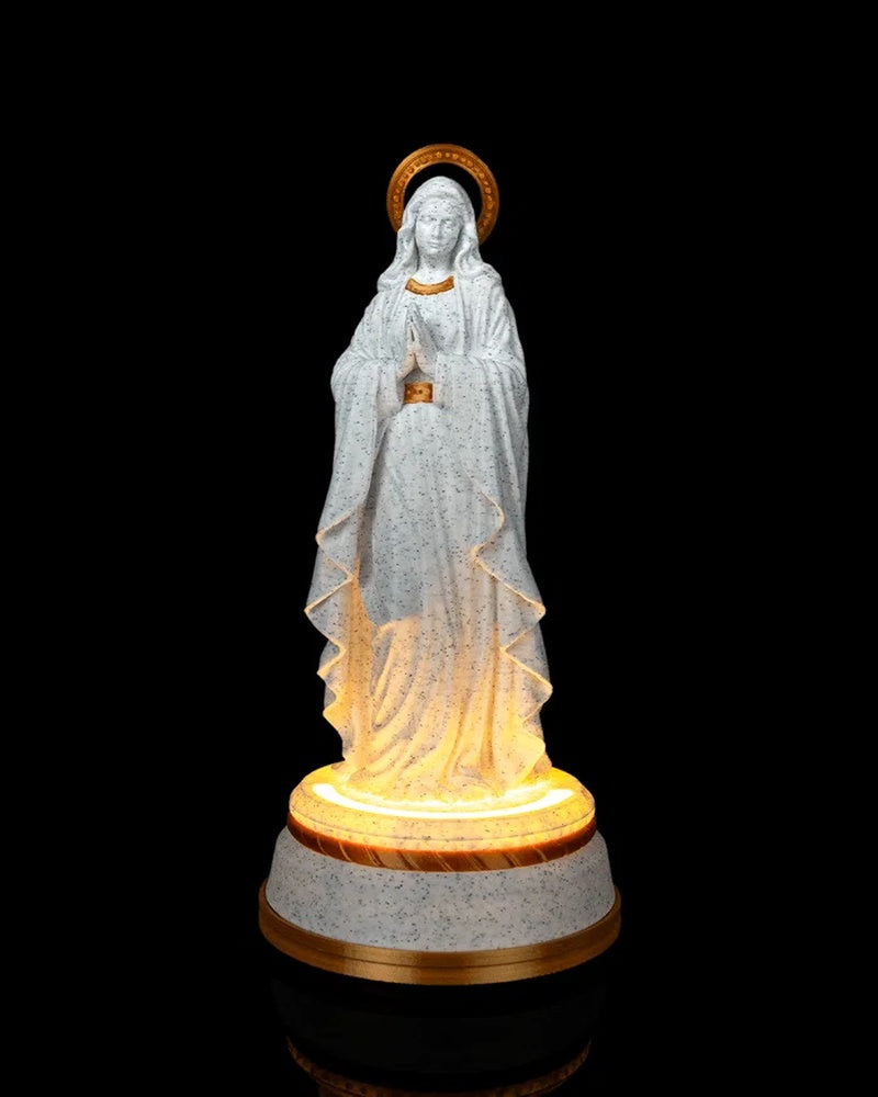 Front view of a white speckled Our Lady statue with gold accents and a glowing base on a black background.