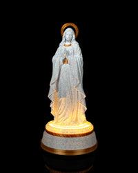 Front view of a white speckled Our Lady statue with gold accents and a glowing base on a black background.