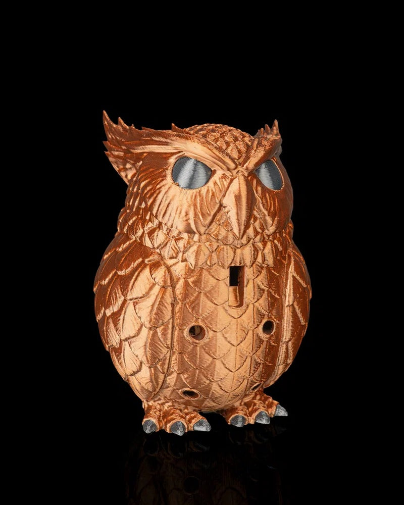 Angled front view of a copper-colored owl figurine with raised feather details, large eyes, a beak and round front openings
