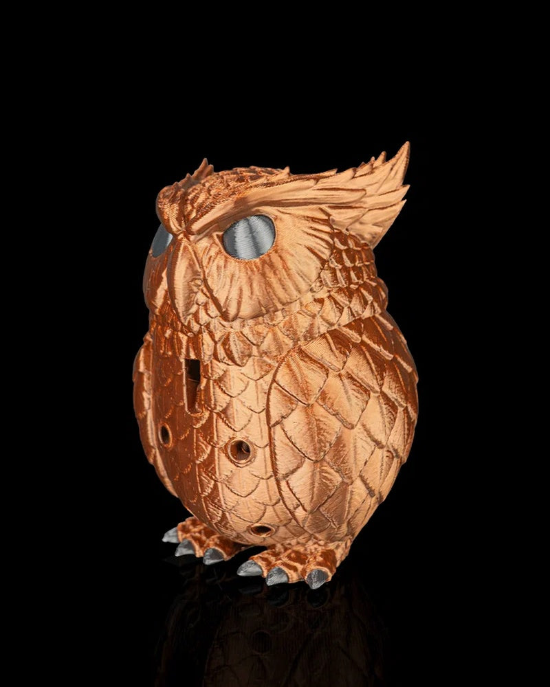 Side view of a copper-colored owl figurine with layered wing and feather texture, silver eyes and gray claws on a black background