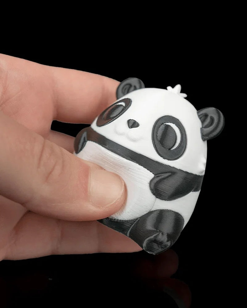 Black-and-white panda figure held between fingers on a dark background