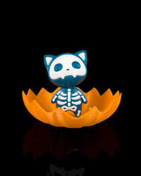 Blue skeleton cat figurine sitting inside an orange jagged pumpkin shell