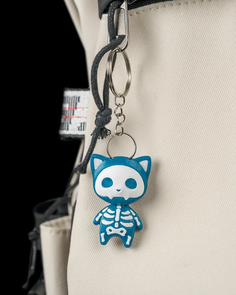 Blue skeleton cat figure hanging from a metal ring and chain on a beige bag