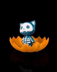 Side view of a blue skeleton cat figurine inside an orange jagged pumpkin shell