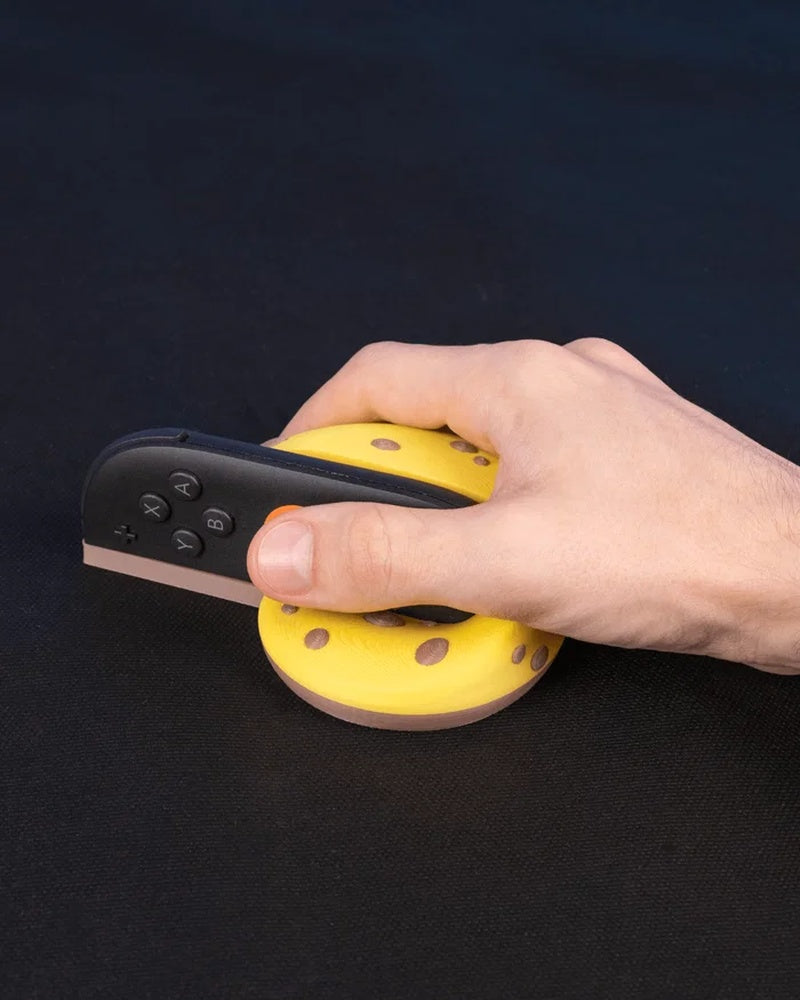 Hand holding a black controller seated in a yellow banana peel shaped grip on a dark surface.