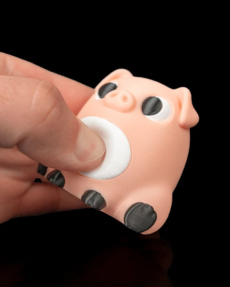 A hand presses the white belly of a peach pig figure with black eyes and dark hooves against a black background.
