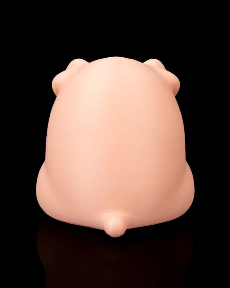 The back of a peach pig figure shows rounded ears, a smooth body, and a small tail on a black reflective surface.