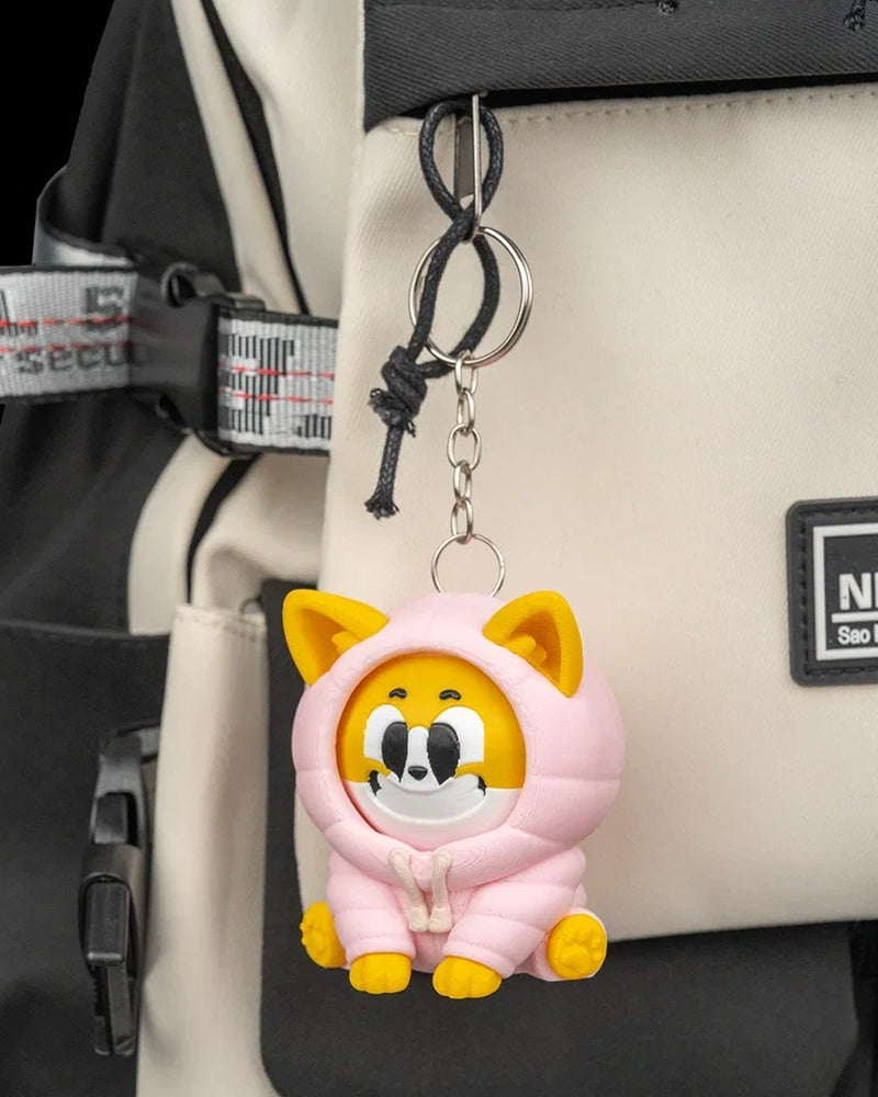 A yellow and white dog figurine in a pink hood hanging from a metal ring on a cream and black bag.