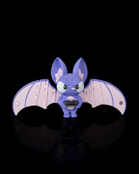 Purple bat figurine with pale pink wings holding a small black controller on a black background