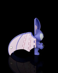 Side view of a purple bat figurine with a pale pink wing extended on a black background