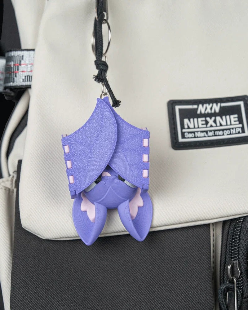 Purple bat character hanging by a ring and cord from a light-colored bag