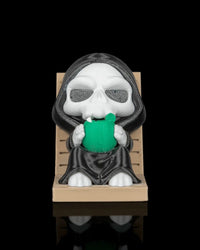 Front view of a hooded skull character seated on a tan lounge chair holding a green drink