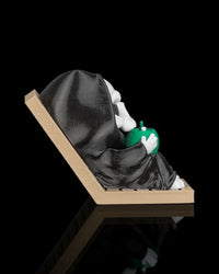 Side view of a hooded skull character reclining on a tan lounge chair while holding a green drink