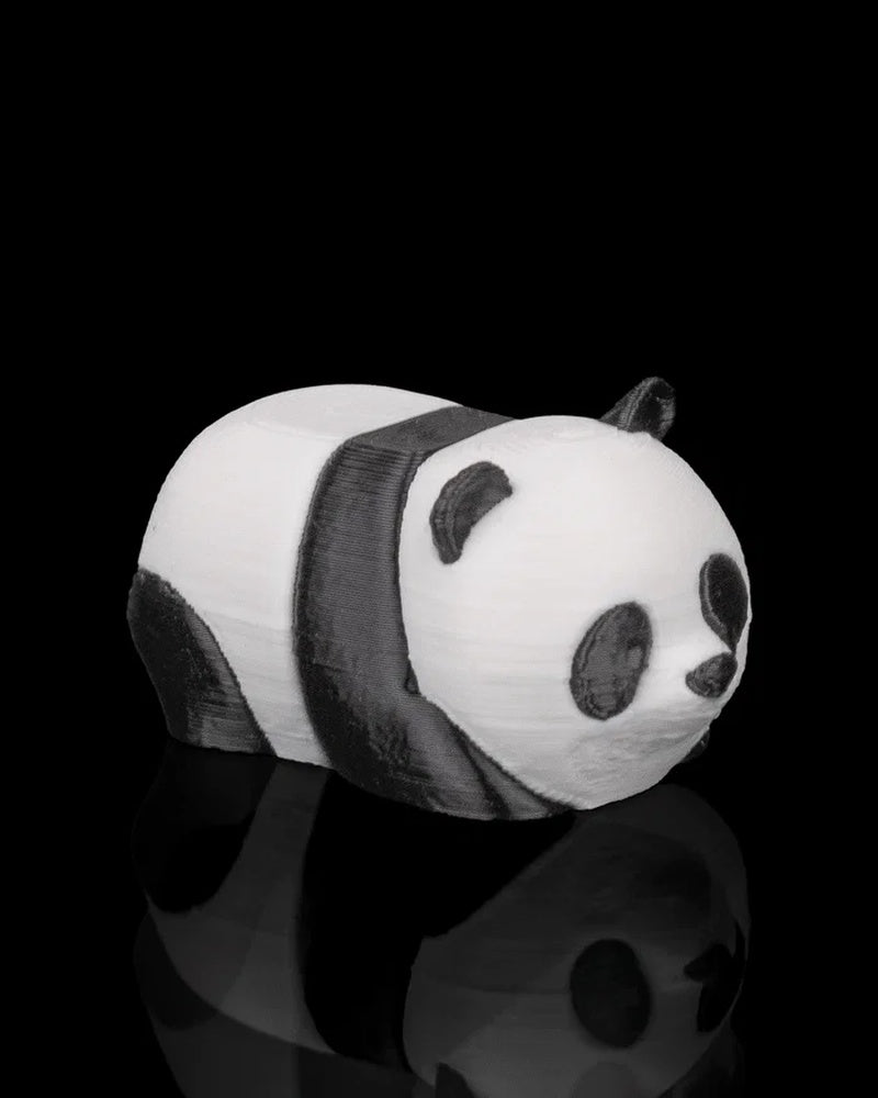 Side view of a black-and-white panda figurine in a resting pose on a dark surface