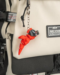 Orange dragon charm hanging by a metal ring and chain from a beige bag