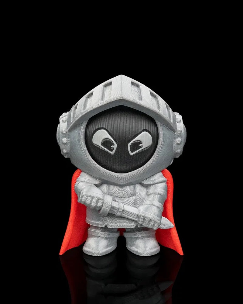 Front view of a small silver knight character with a black face, white eyes, and red cape on a black background