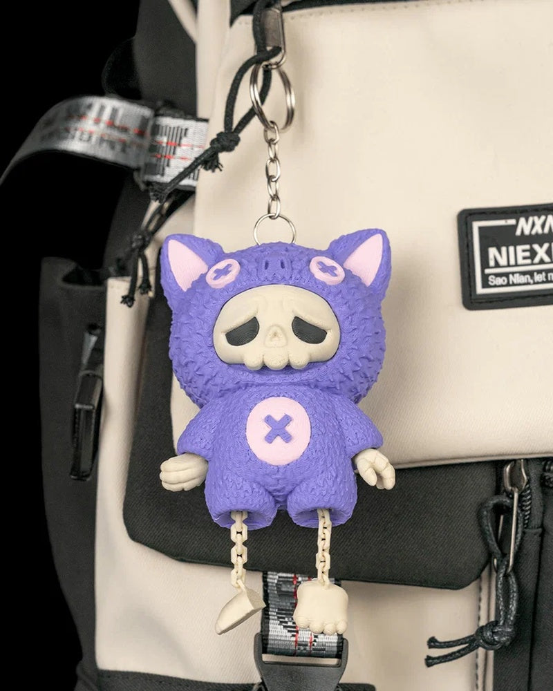 Purple bat-themed skull figure hanging from a metal ring and chain against a bag