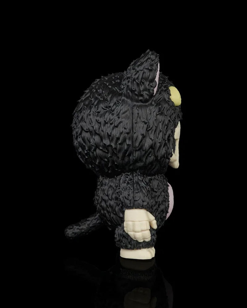 Side view of a black cat skull figurine with raised fur texture, pale hand, tail, and one yellow eye visible