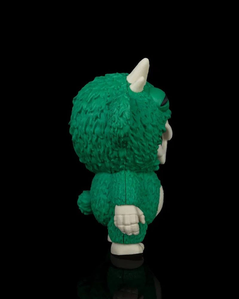 Side view of a green monster toy with white horn and hand on a black background