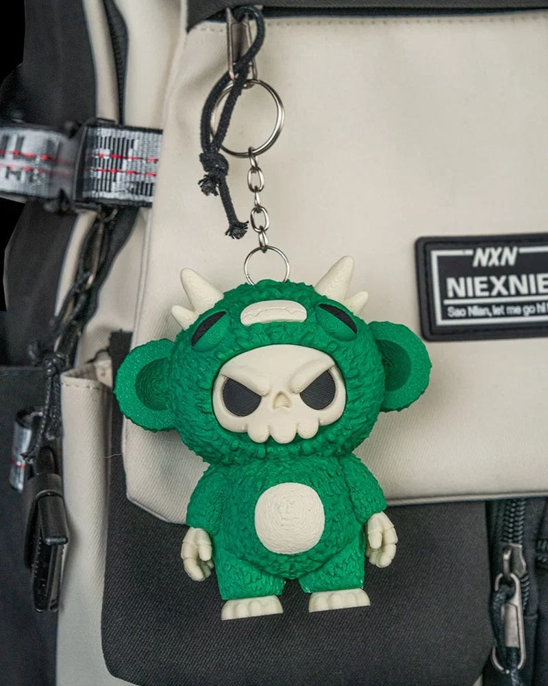 Green skull-faced monster toy hanging from a ring and chain on a bag