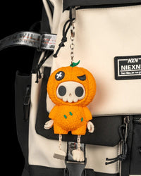 Orange pumpkin skull charm hanging from a cream and black bag