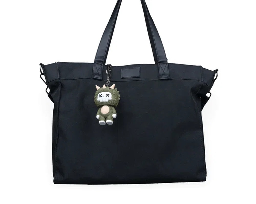 Small horned dinosaur character hanging from a black tote bag by a metal chain.