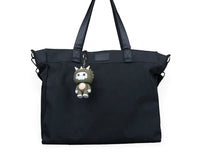 Small horned dinosaur character hanging from a black tote bag by a metal chain.