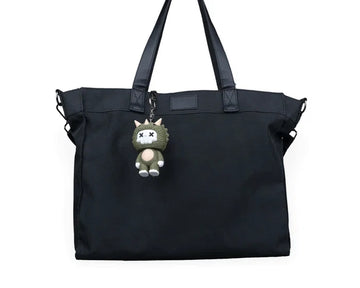 Small horned dinosaur character hanging from a black tote bag by a metal chain.