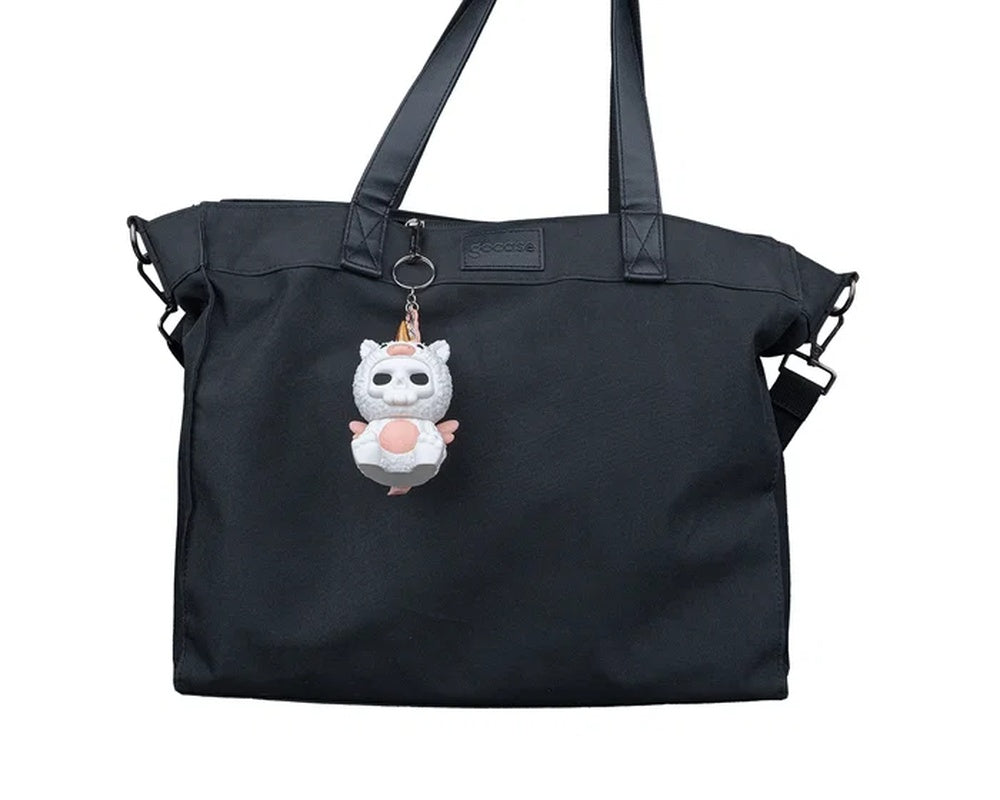 Small white unicorn costume figure hanging from a black bag by a metal ring