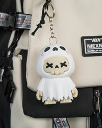 White ghost skull figurine hanging from a metal ring and chain against a beige and black bag.
