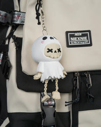 Angled view of the white ghost skull figurine hanging from a metal ring and chain against a beige and black bag.