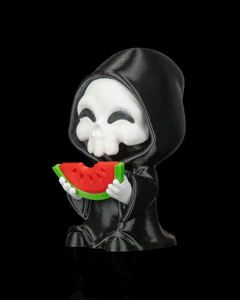 Side view of a hooded skull figurine holding a watermelon slice on a black background