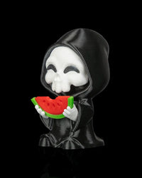Side view of a hooded skull figurine holding a watermelon slice on a black background
