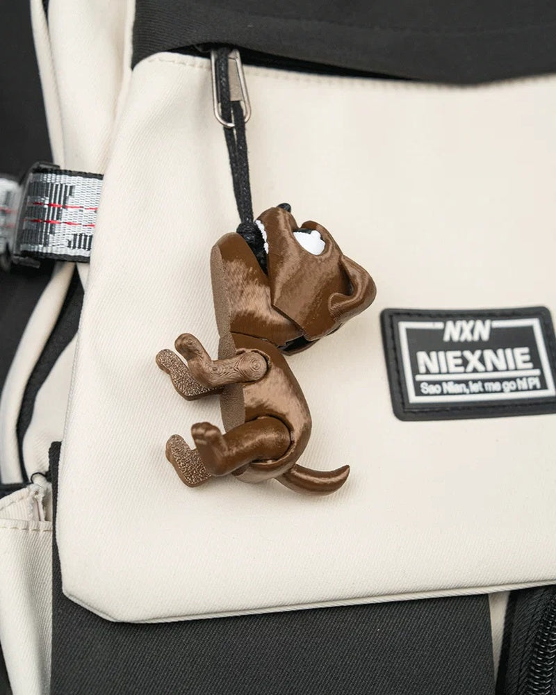 Brown puppy toy hanging by a visible black loop from a light-colored bag