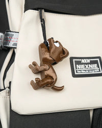 Brown puppy toy hanging by a visible black loop from a light-colored bag