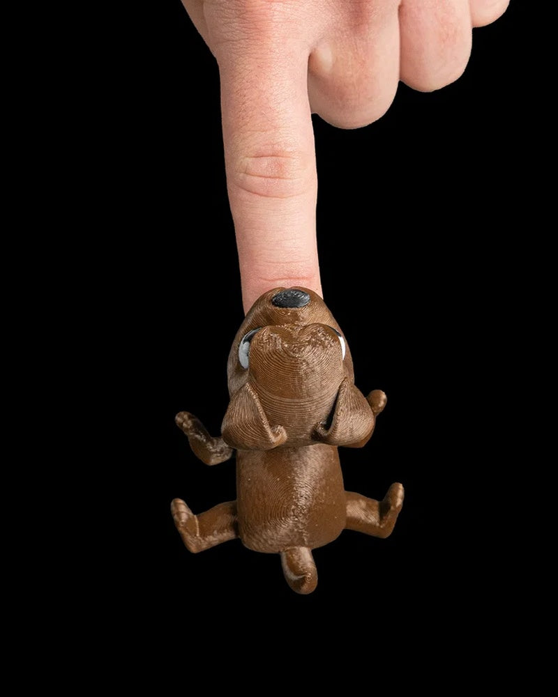 Top view of a finger pressing the nose of a brown puppy toy on a black background