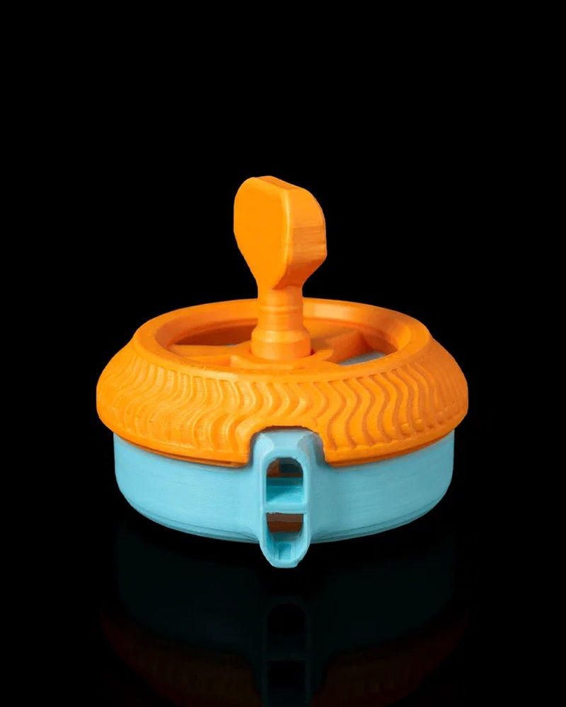 Orange and blue circular toy with a raised top grip and front whistle-shaped opening on a black background