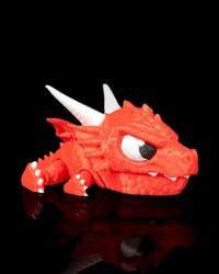Red dragon toy with white horns, teeth, claws, and wings on a black reflective surface