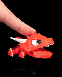 Red dragon toy with its mouth open while a finger presses the top of its head