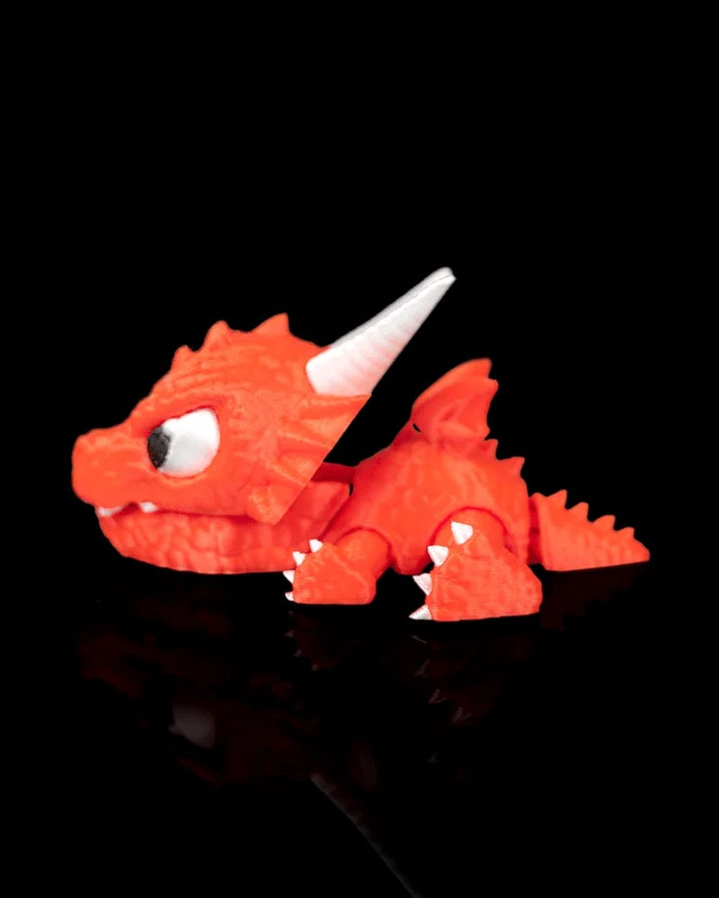Side view of a red dragon toy with a white horn, wing, teeth, and tail on a black surface