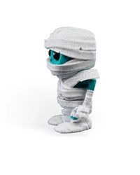 Right side view of a white wrapped monster figurine with large black eyes and turquoise arm details.