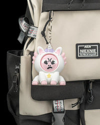 White unicorn axolotl character hanging from a metal ring and chain on a beige and black backpack