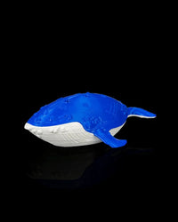 Blue and white whale figurine on a black reflective surface viewed from the side