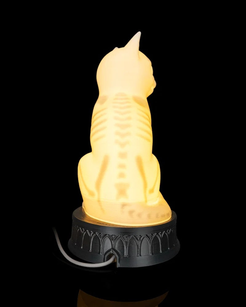Rear view of a glowing cat-shaped lamp with a white cord behind the base