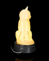 Rear view of a glowing cat-shaped lamp with a white cord behind the base